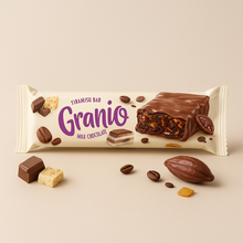 A light-colored Granio Tiramisu snack bar covered in milk chocolate, surrounded by coffee beans, a cocoa pod, and small chocolate pieces on a clean background.